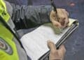 Policía rellenando multa de tráfico por no llevar carné de conducir.
