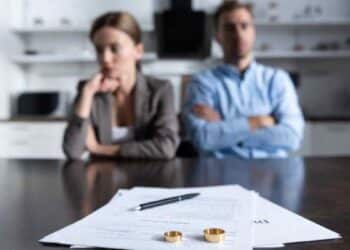 Pareja en proceso de divorcio con documentos y anillos sobre la mesa.