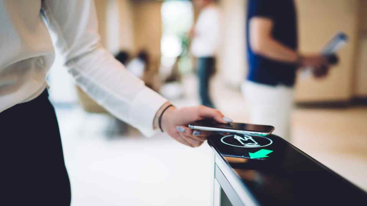 Empleado fichando jornada laboral con móvil en torno de acceso.