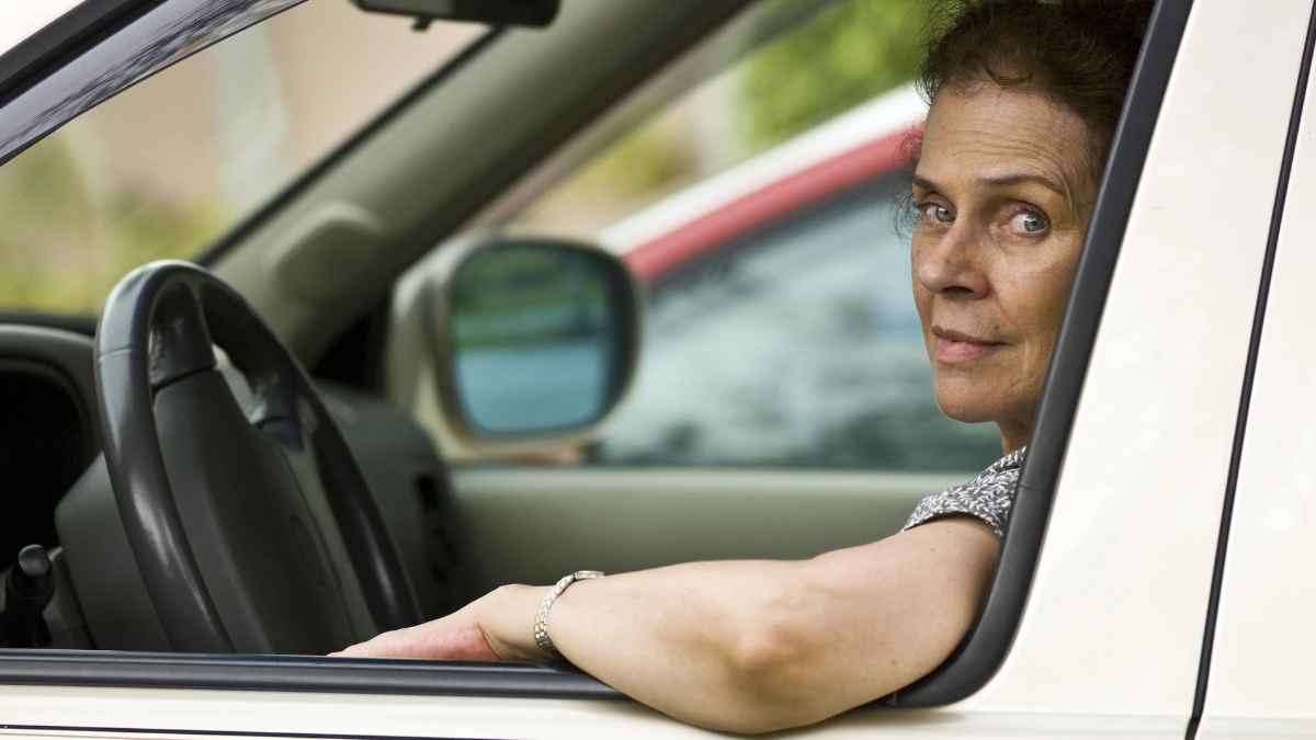 Mujer conduciendo con el brazo apoyado en la ventanilla del coche.