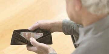Hombre mayor revisando cartera con poco dinero por devolver IMV.