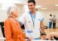 Anciana en residencia con cuidador sanitario en sala de ejercicios.