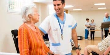 Anciana en residencia con cuidador sanitario en sala de ejercicios.