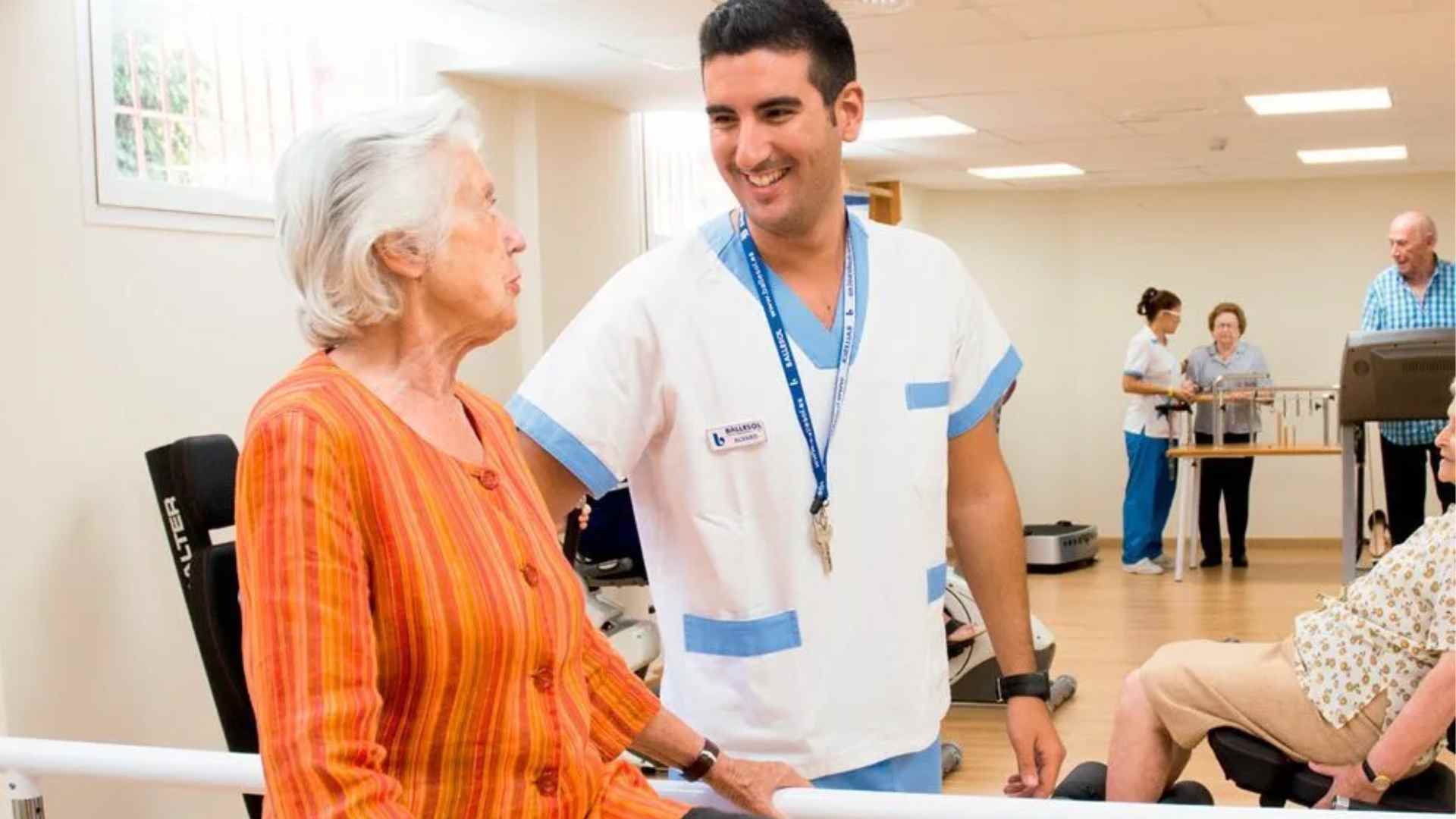 Anciana en residencia con cuidador sanitario en sala de ejercicios.