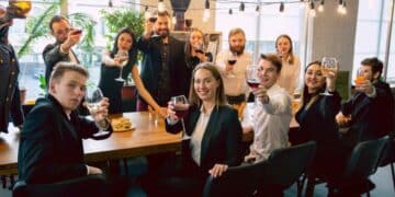 Trabajadores en fiesta de empresa con copas de vino y alcohol.