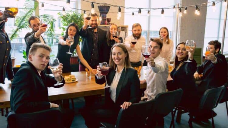 Trabajadores en fiesta de empresa con copas de vino y alcohol.