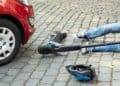 Trabajador en patinete eléctrico accidentado frente a coche en vía urbana.