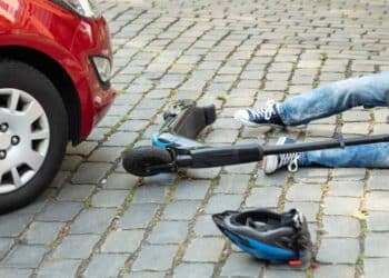 Trabajador en patinete eléctrico accidentado frente a coche en vía urbana.