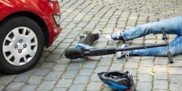 Trabajador en patinete eléctrico accidentado frente a coche en vía urbana.