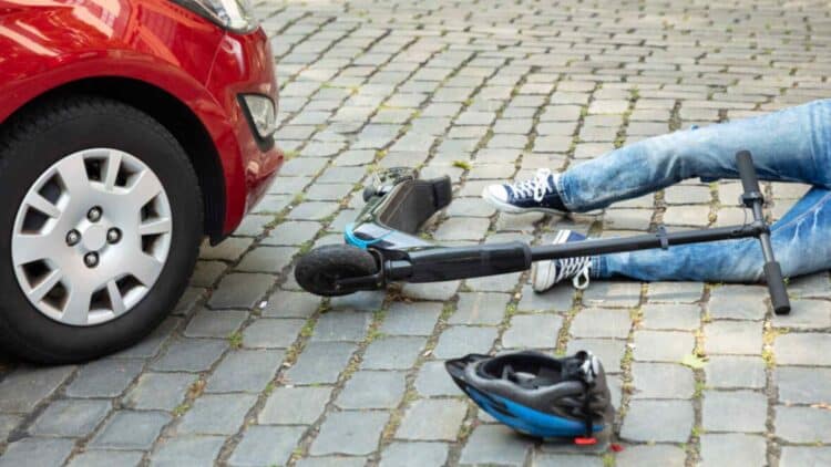 Trabajador en patinete eléctrico accidentado frente a coche en vía urbana.