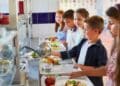 Niños en comedor escolar con bandejas de comida durante la vuelta al cole.
