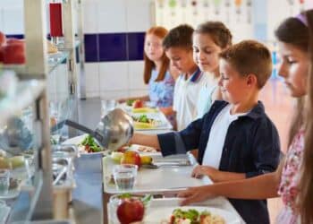 Niños en comedor escolar con bandejas de comida durante la vuelta al cole.