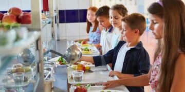 Niños en comedor escolar con bandejas de comida durante la vuelta al cole.