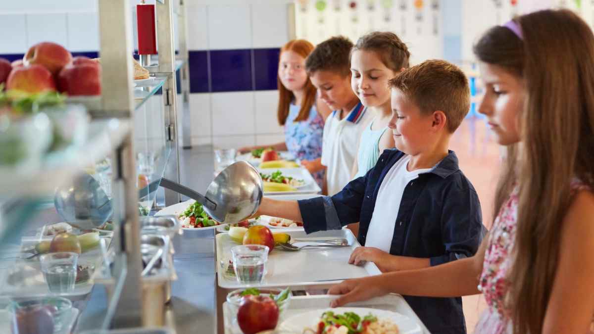 Niños en comedor escolar con bandejas de comida durante la vuelta al cole.