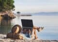 Empleado teletrabajando con portátil en la playa durante sus vacaciones.