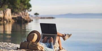 Empleado teletrabajando con portátil en la playa durante sus vacaciones.