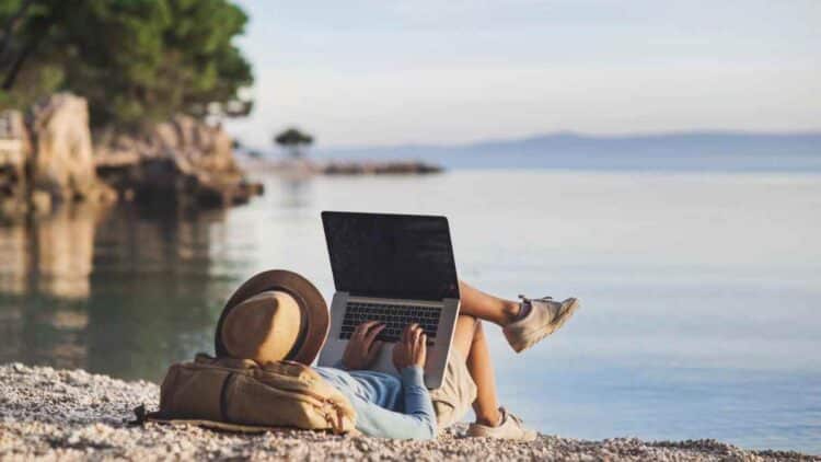 Empleado teletrabajando con portátil en la playa durante sus vacaciones.