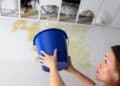 Mujer colocando un cubo bajo gotera en el techo según la Ley de Propiedad Horizontal.