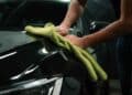 Persona limpiando un coche en concesionario de Madrid con paño de microfibra verde.