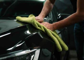 Persona limpiando un coche en concesionario de Madrid con paño de microfibra verde.