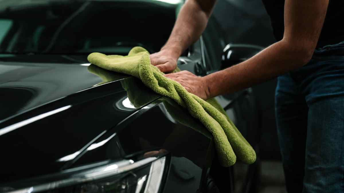 Persona limpiando un coche en concesionario de Madrid con paño de microfibra verde.