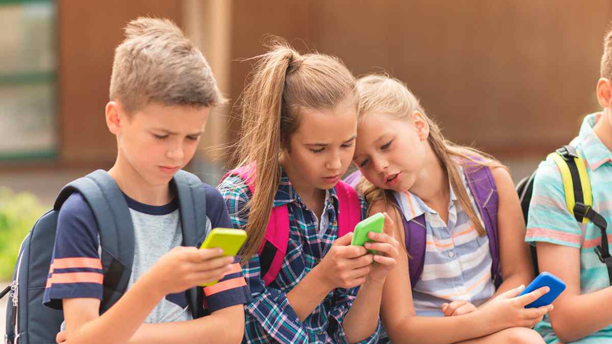 niños usando el móvil en la puerta del colegio antes de los 16 años