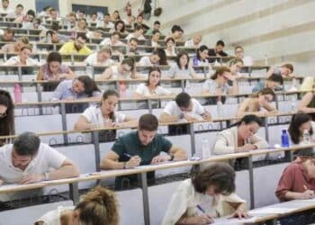 Personas realizando examen de oposiciones en un aula universitaria.