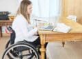 Mujer en silla de ruedas trabajando con portátil sobre pensión de incapacidad permanente.