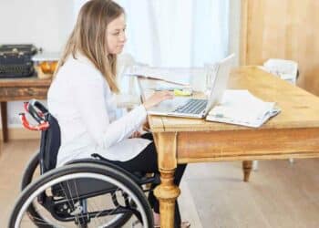 Mujer en silla de ruedas trabajando con portátil sobre pensión de incapacidad permanente.