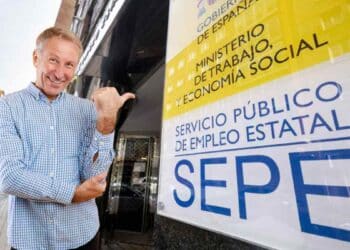 Hombre mayor señalando cartel del SEPE sobre subsidio de 482 euros para mayores de 52 años.
