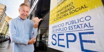 Hombre mayor señalando cartel del SEPE sobre subsidio de 482 euros para mayores de 52 años.