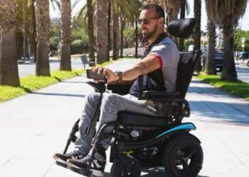 Persona con discapacidad usando silla de ruedas eléctrica por la calle para ilustrar ayudas MUGEJU 2025.