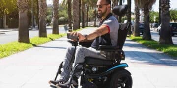 Persona con discapacidad usando silla de ruedas eléctrica por la calle para ilustrar ayudas MUGEJU 2025.