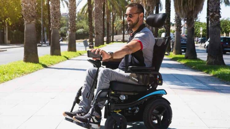 Persona con discapacidad usando silla de ruedas eléctrica por la calle para ilustrar ayudas MUGEJU 2025.