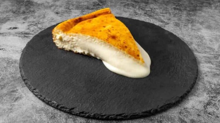Porción de tarta de queso cremosa de Bascake Madrid sobre base de pizarra negra.