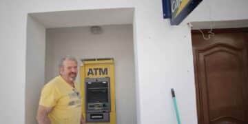 Hombre junto a cajero automático multimarca en un pueblo