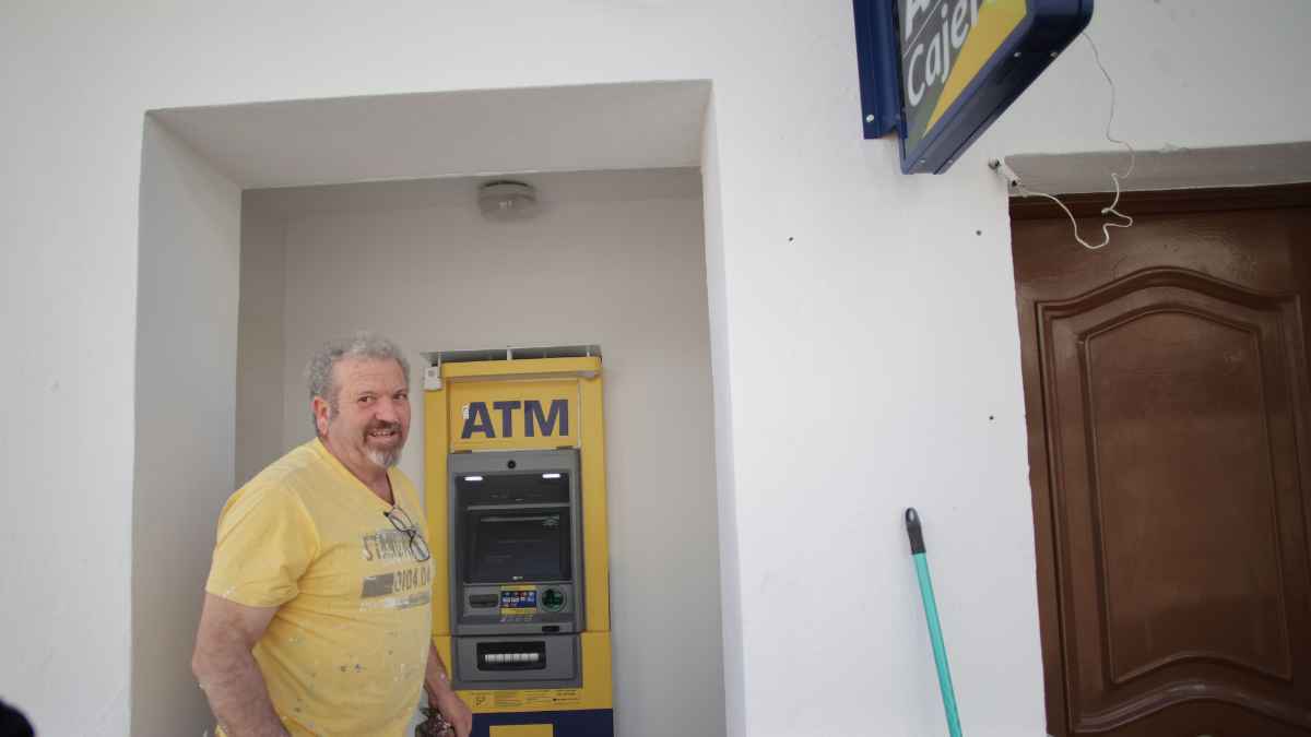 Hombre junto a cajero automático multimarca en un pueblo