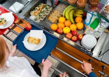 Alumnos en comedor escolar con bandejas y frutas frescas en Madrid.