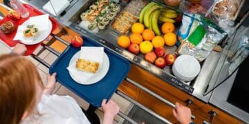 Alumnos en comedor escolar con bandejas y frutas frescas en Madrid.