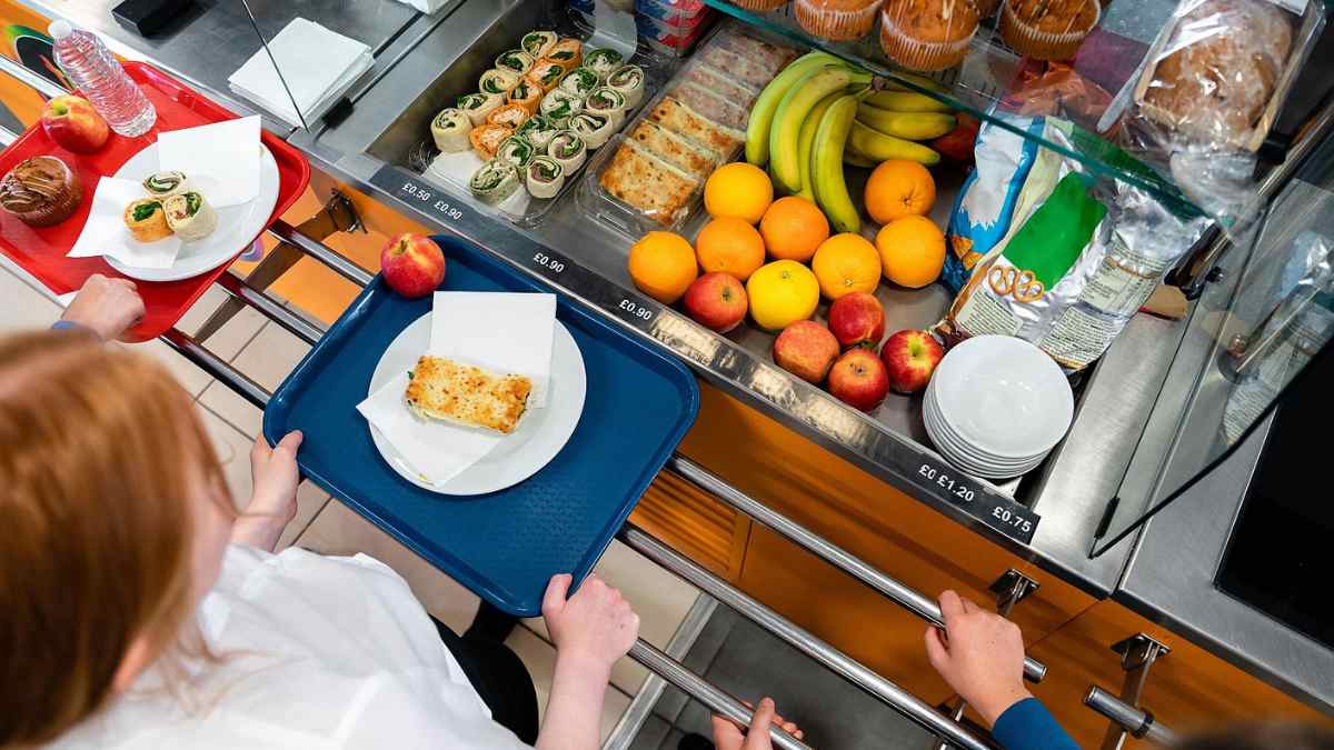 Alumnos en comedor escolar con bandejas y frutas frescas en Madrid.