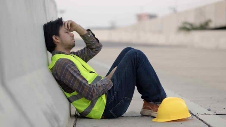 Trabajador agotado en pausa laboral, Estatuto de los Trabajadores garantiza descansos diarios y semanales mínimos.