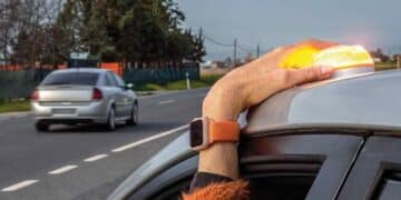 conductor colocando luz v16 en el techo del coche en carretera.