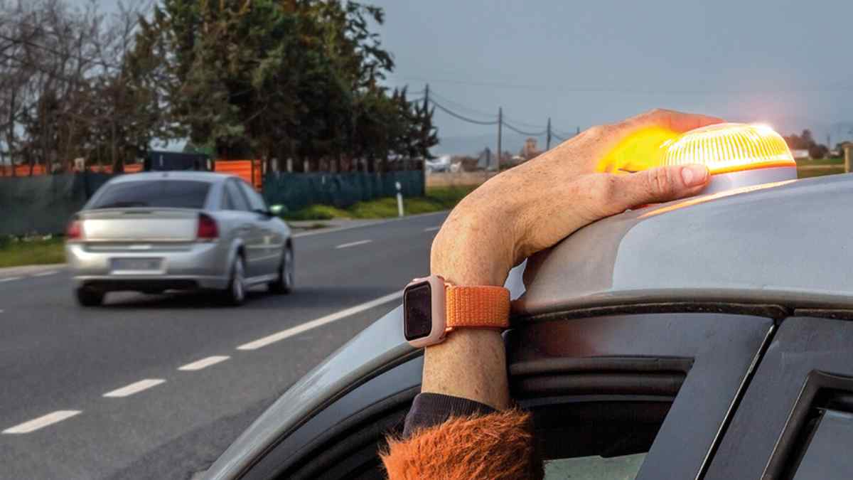 conductor colocando luz v16 en el techo del coche en carretera.