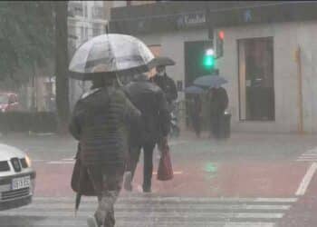Personas con paraguas caminando bajo la lluvia en Madrid durante las lluvias pasajeras anunciadas por la Aemet.