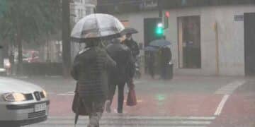 Personas con paraguas caminando bajo la lluvia en Madrid durante las lluvias pasajeras anunciadas por la Aemet.