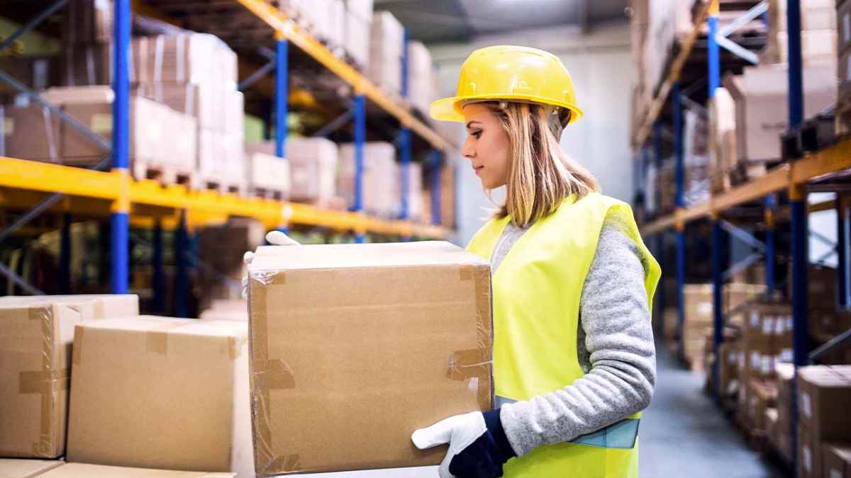 Mozo de almacén trabajando en un centro logístico de Madrid con cajas y uniforme de seguridad.