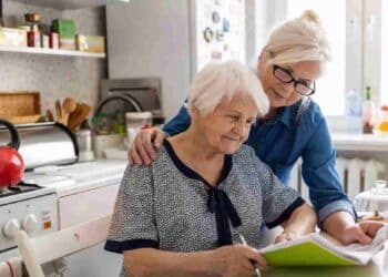 Mujer mayor y cuidadora revisando documentos sobre pensión de orfandad mayores de 52 años.