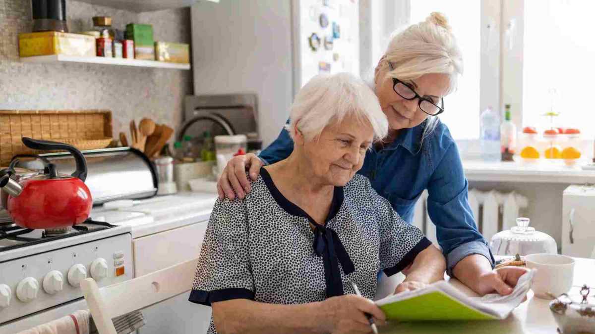 Mujer mayor y cuidadora revisando documentos sobre pensión de orfandad mayores de 52 años.