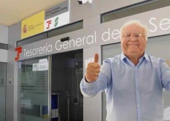 Jubilado feliz frente a la Tesorería General de la Seguridad Social tras aumento de pensión mínima por cambio familiar.
