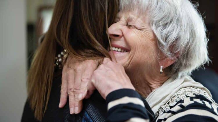 Mujer mayor sonriendo al abrazar tras recibir el subsidio indefinido de 480 euros del SEPE.
